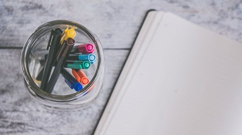 Pens in a jar beside a notebook